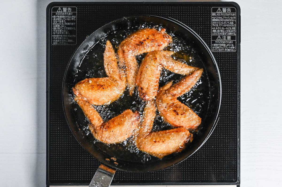 golden chicken wings shallow frying in a pan