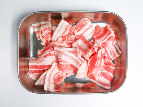thinly sliced pork belly sprinkled with salt and pepper in a metal container