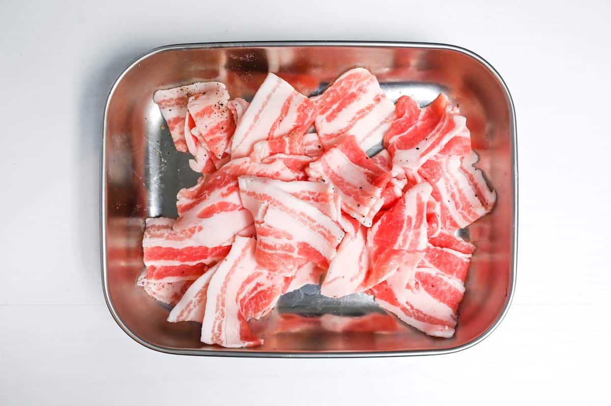 thinly sliced pork belly sprinkled with salt and pepper in a metal container