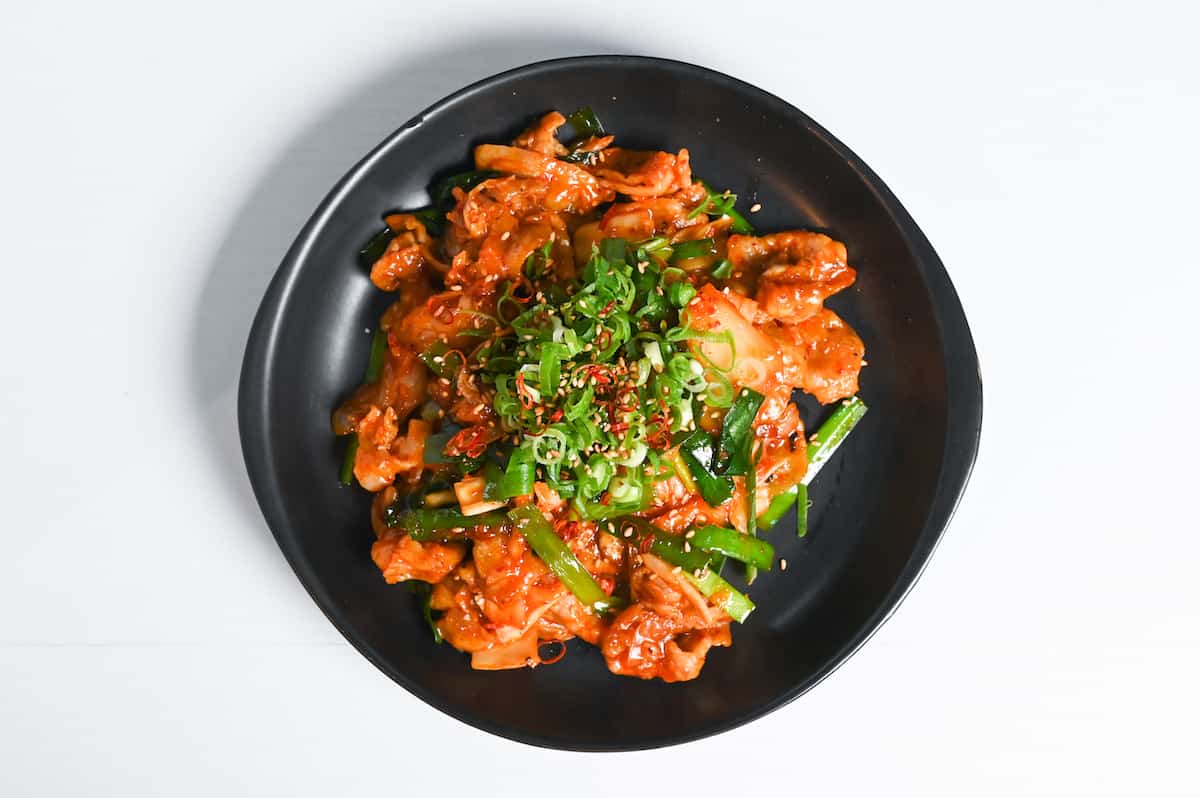 Japanese style buta kimchi itame on a black plate on a white background