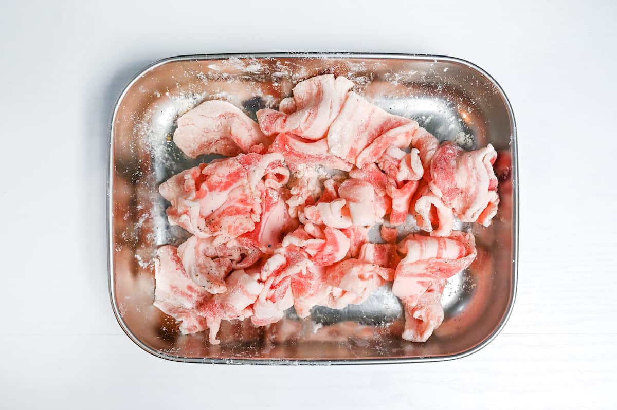thinly sliced pork belly coated with cake flour in a metal container
