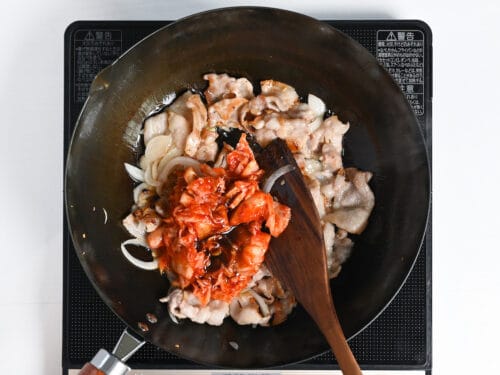 Adding kimchi to the wok to make buta kimchi itame
