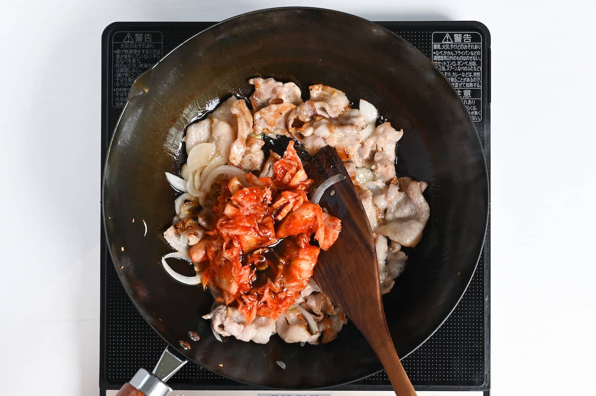 Adding kimchi to the wok to make buta kimchi itame