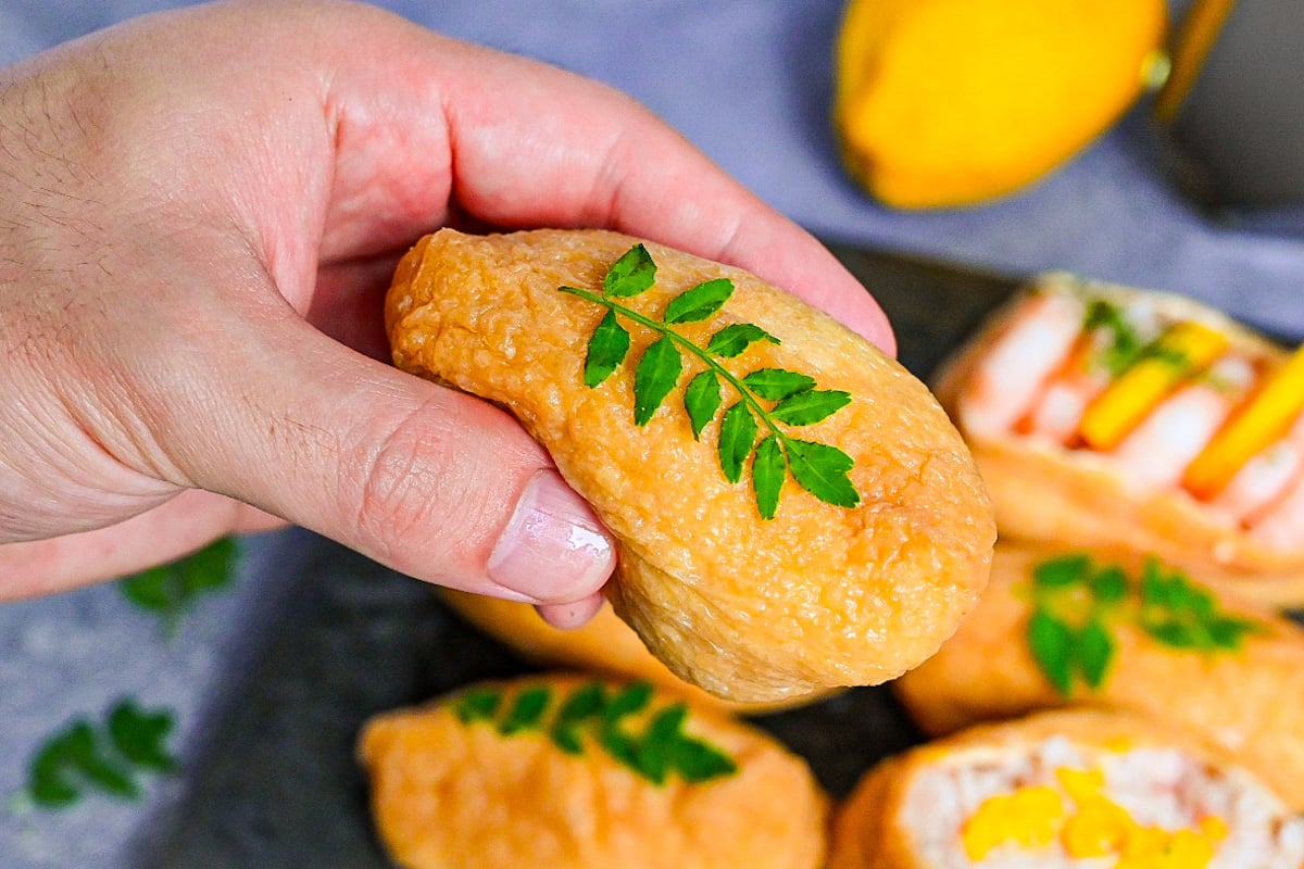 Holding inarizushi in hand topped with edible leaves