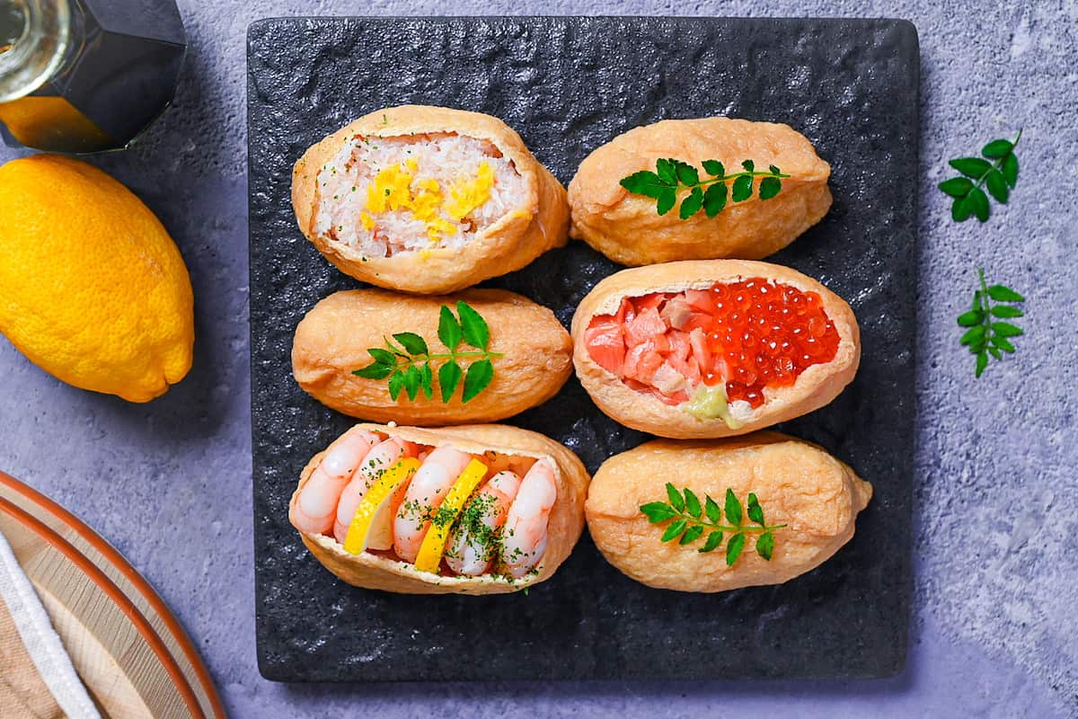 Inarizushi (inari sushi/ stuffed tofu touches) with various toppings on a slate style square plate - top down view