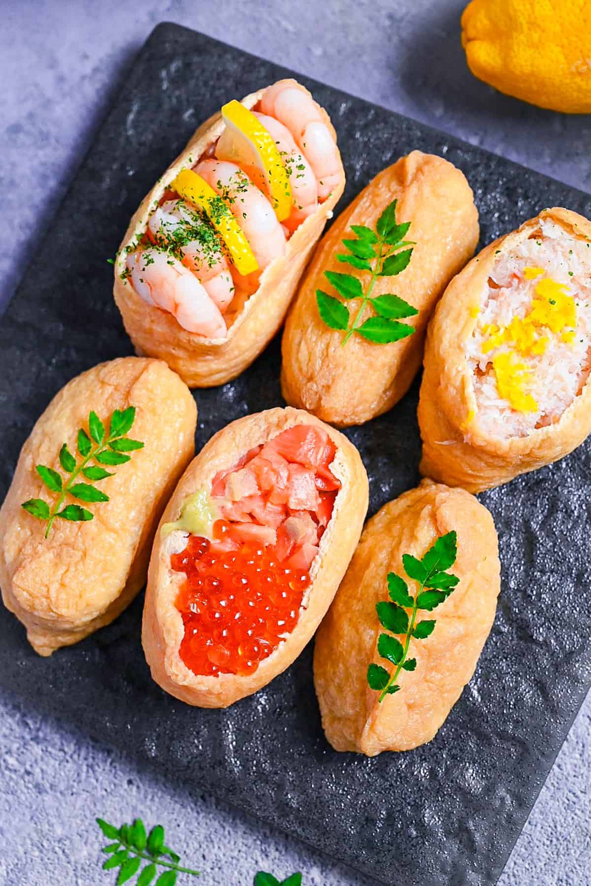 Inarizushi (inari sushi/ stuffed tofu touches) with various toppings on a slate style square plate