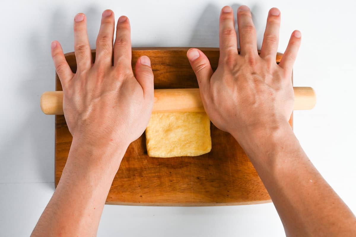 rolling aburaage (fried tofu pouch) with rolling pin on a wooden chopping board