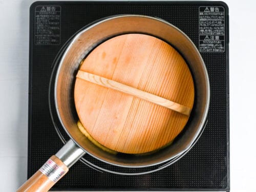 Aburaage topped with wooden drop lid in a sauce pan