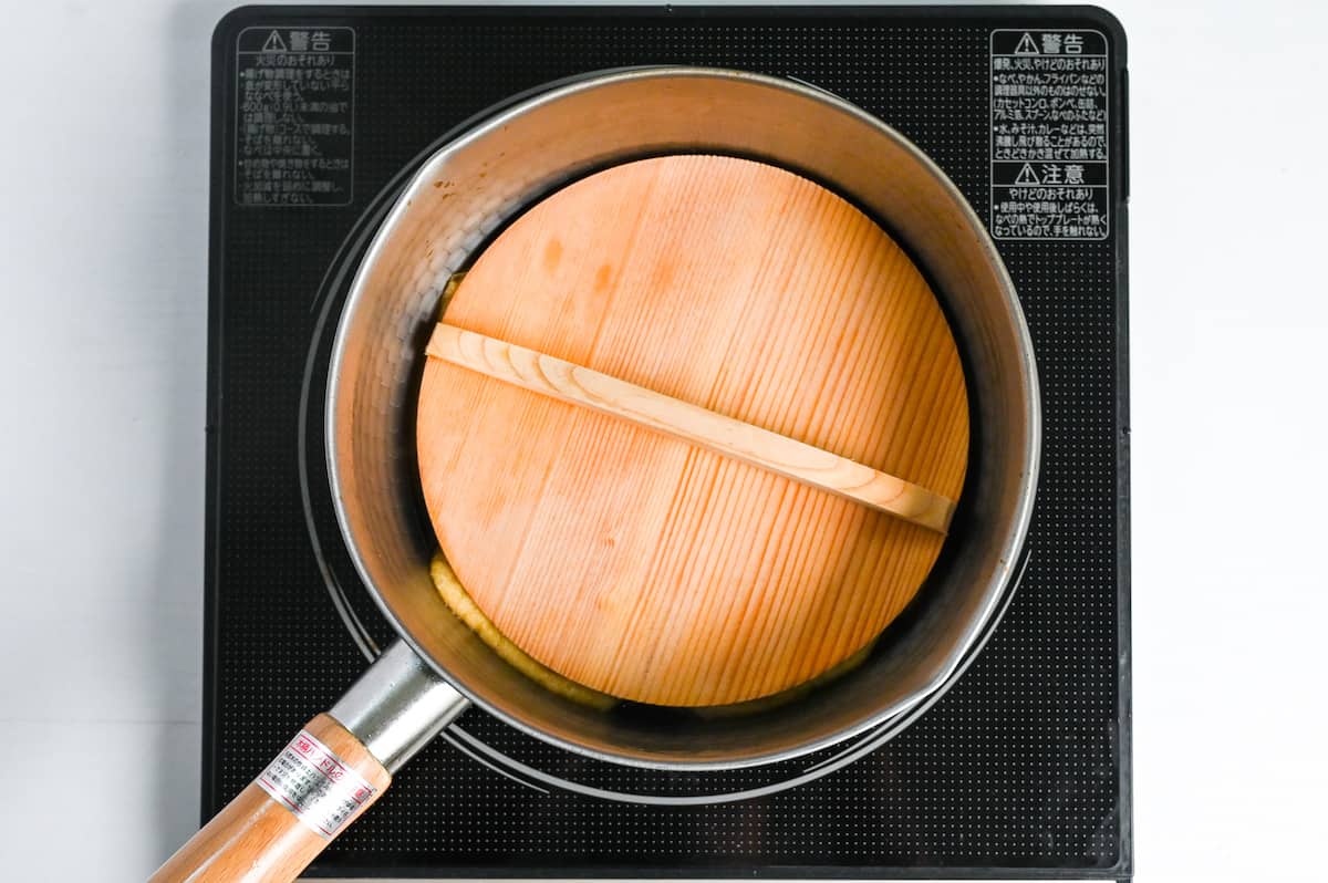 Aburaage topped with wooden drop lid in a sauce pan
