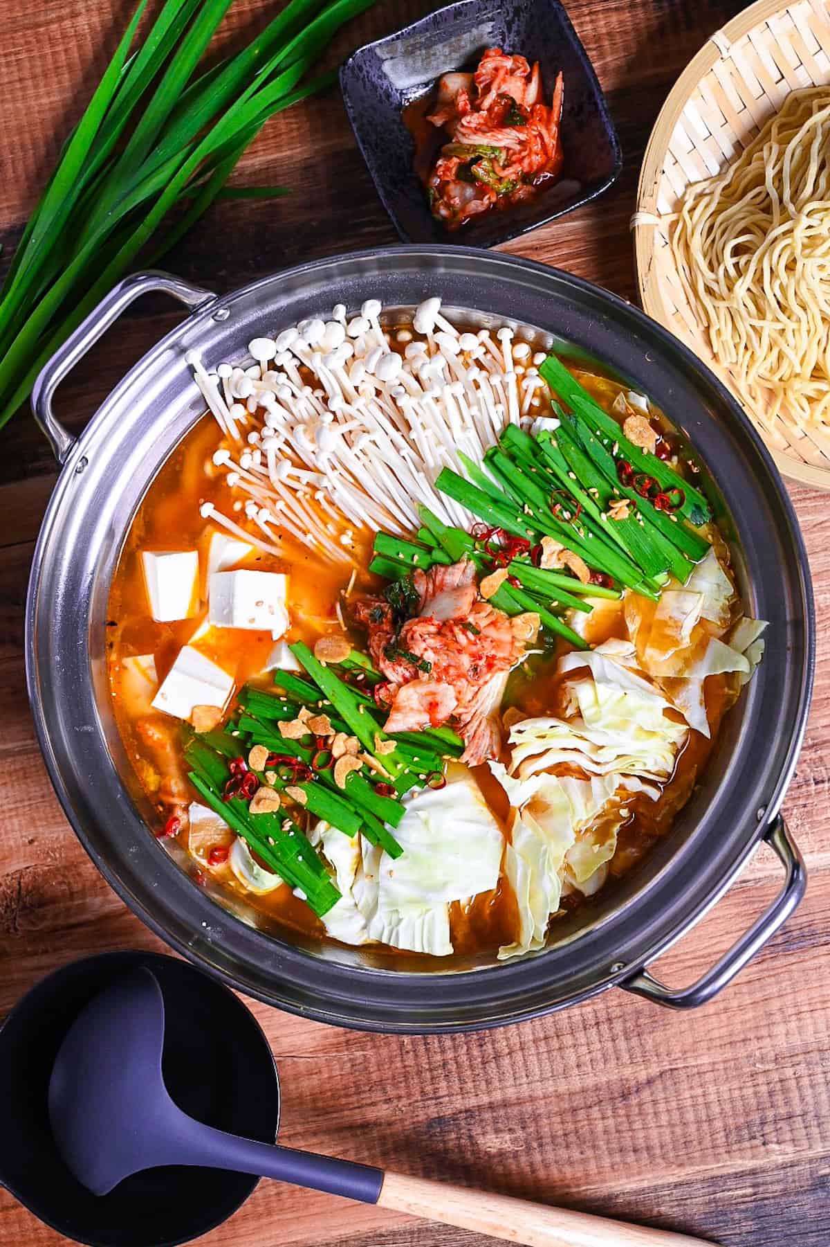 Japanese kimchi nabe with pork, tofu, mushrooms and cabbage topped with garlic chives, fried garlic and chili in an aluminum pot