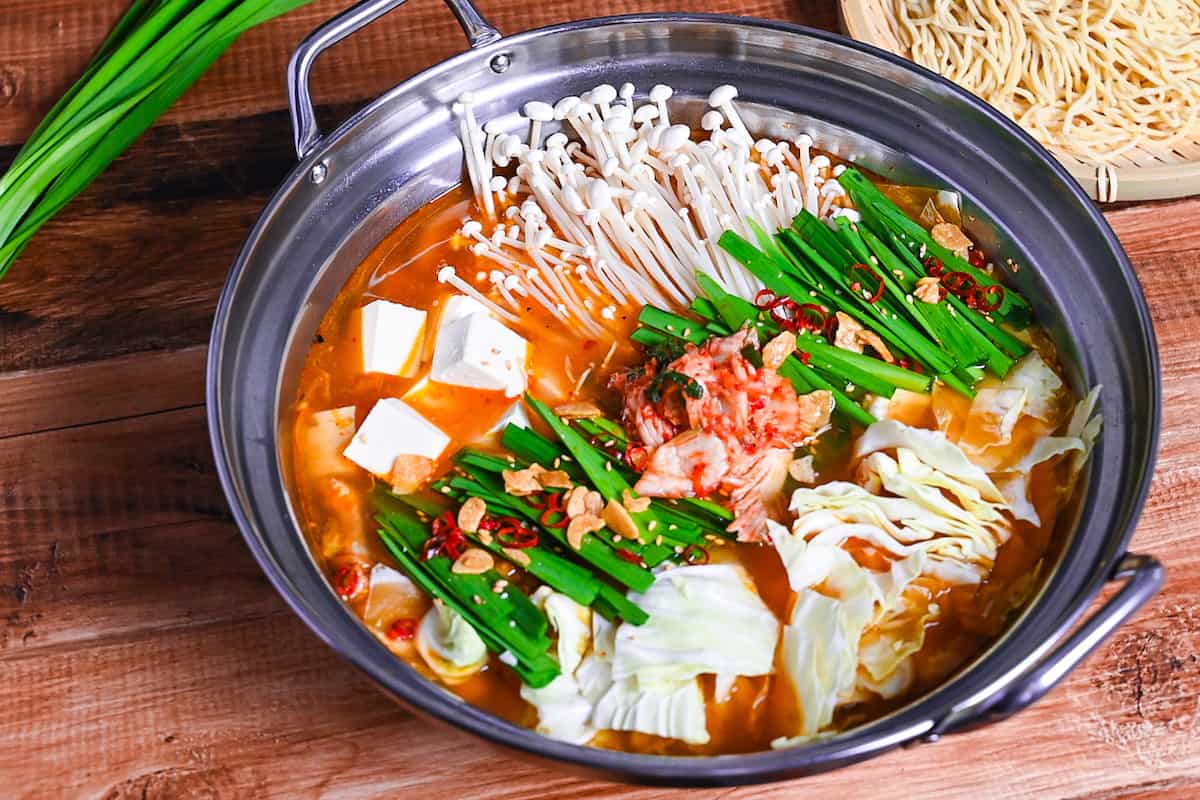 Japanese kimchi nabe with pork, tofu, mushrooms and cabbage topped with garlic chives, fried garlic and chili in an aluminum pot