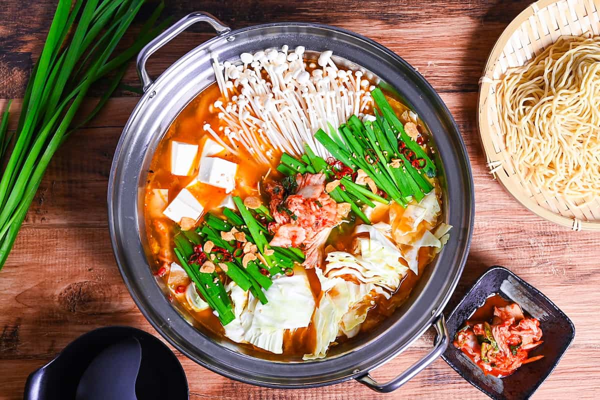 Japanese kimchi nabe with pork, tofu, mushrooms and cabbage topped with garlic chives, fried garlic and chili in an aluminum pot