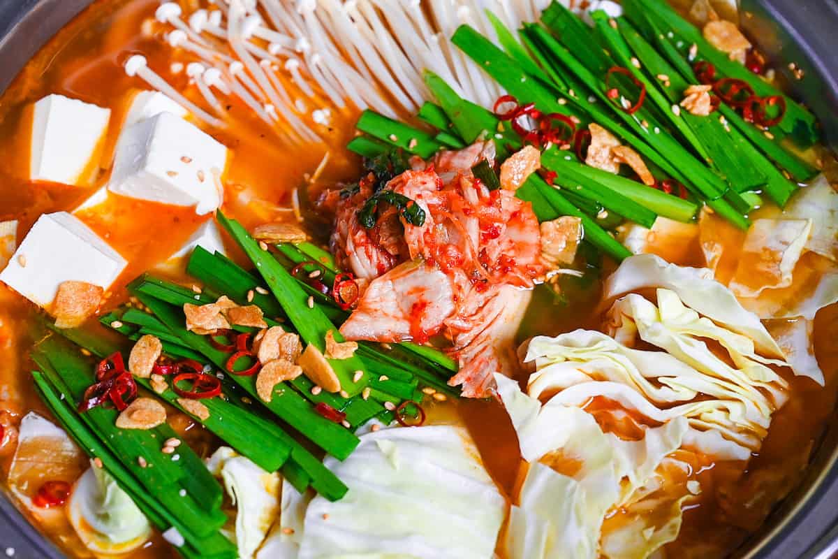 Japanese kimchi nabe with pork, tofu, mushrooms and cabbage topped with garlic chives, fried garlic and chili in an aluminum pot