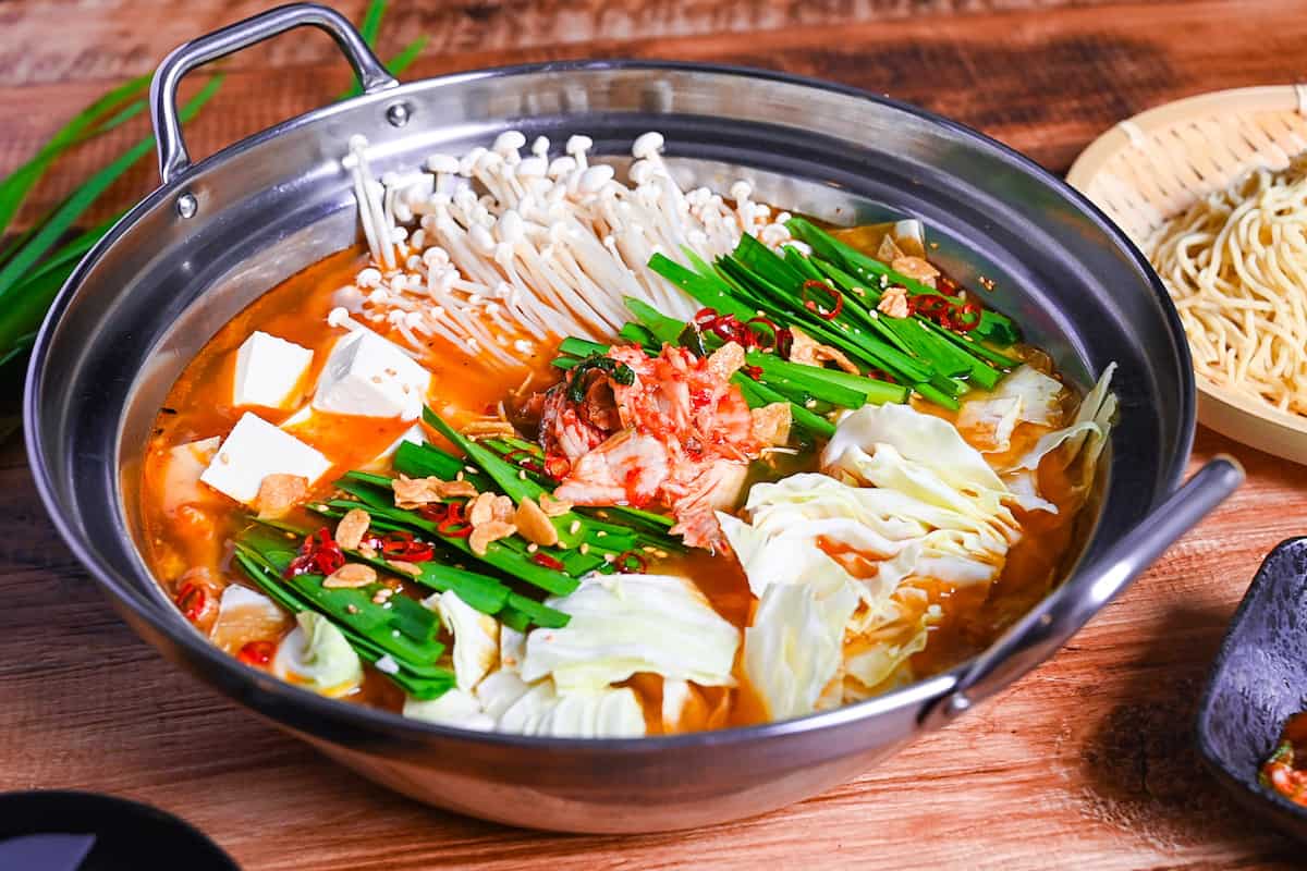 Japanese kimchi nabe with pork, tofu, mushrooms and cabbage topped with garlic chives, fried garlic and chili in an aluminum pot