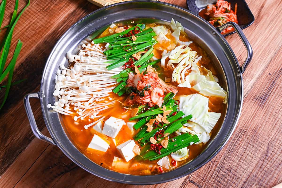 Japanese kimchi nabe with pork, tofu, mushrooms and cabbage topped with garlic chives, fried garlic and chili in an aluminum pot