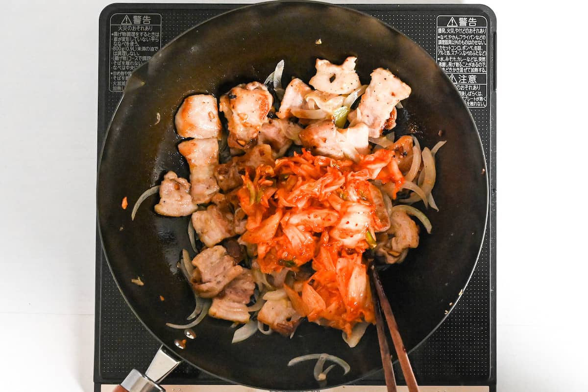 stir-frying pork, onions and kimchi in a wok