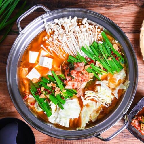 Japanese kimchi nabe with pork, tofu, mushrooms and cabbage topped with garlic chives, fried garlic and chili in an aluminum pot