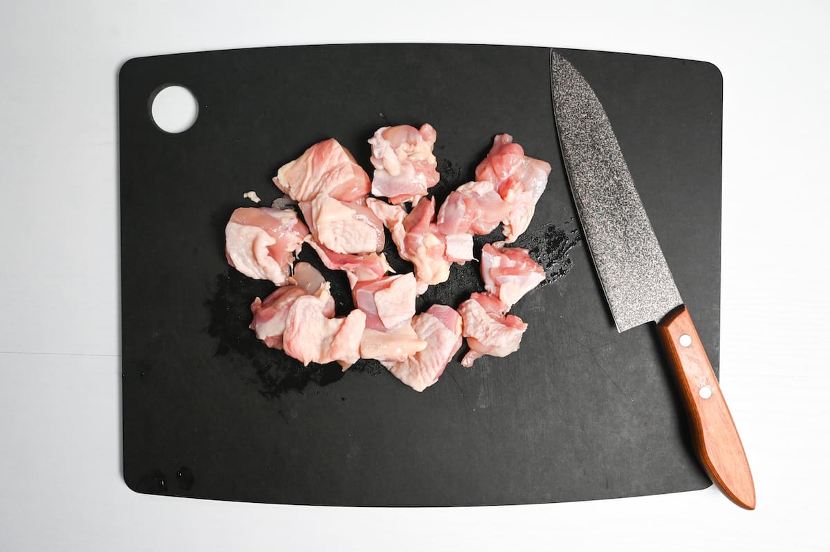 chicken thigh cut into bitesize pieces on a black chopping board