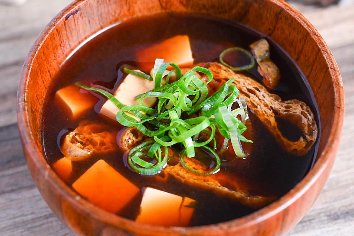 close up of aka-dashi (red miso soup) in wooden bowl topped with chopped green onion