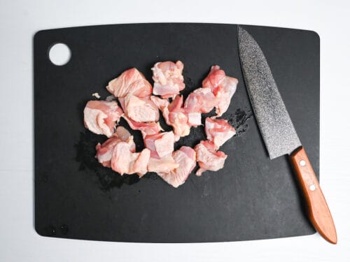 pieces of skin-on chicken thigh cut into bite-size pieces on a black chopping board
