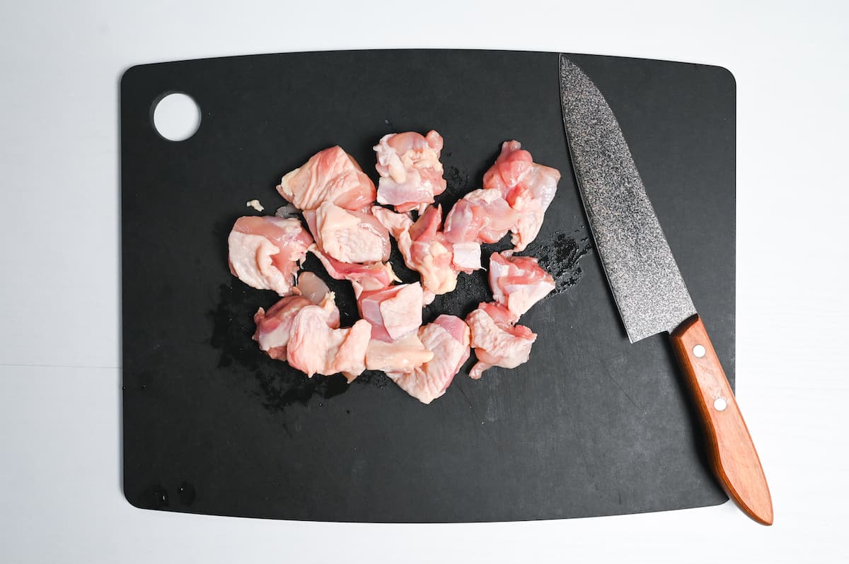 pieces of skin-on chicken thigh cut into bite-size pieces on a black chopping board