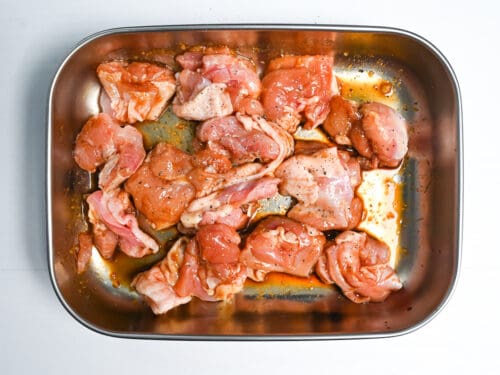 chicken thigh sprinkled with pepper and then coated in marinade in a metal container