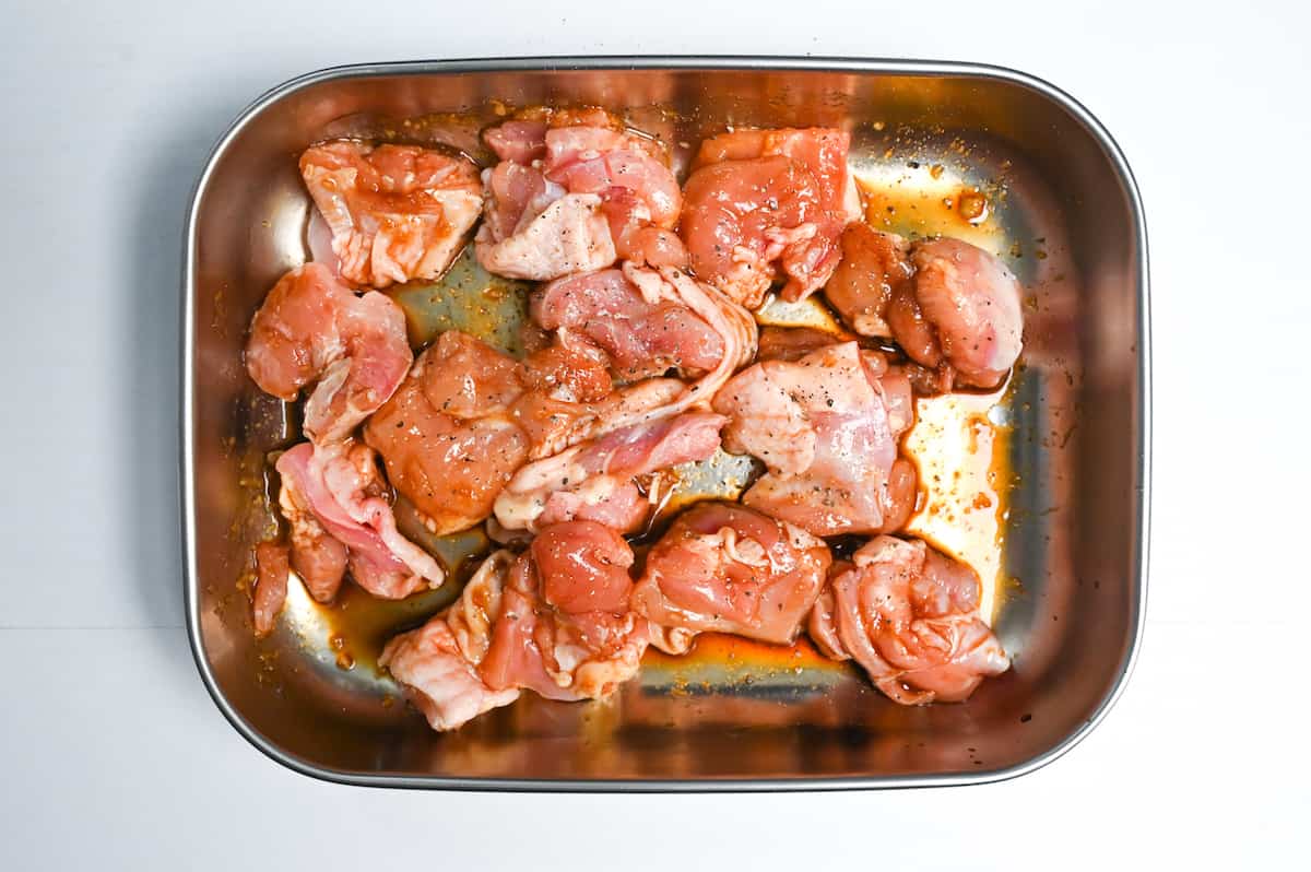 chicken thigh sprinkled with pepper and then coated in marinade in a metal container