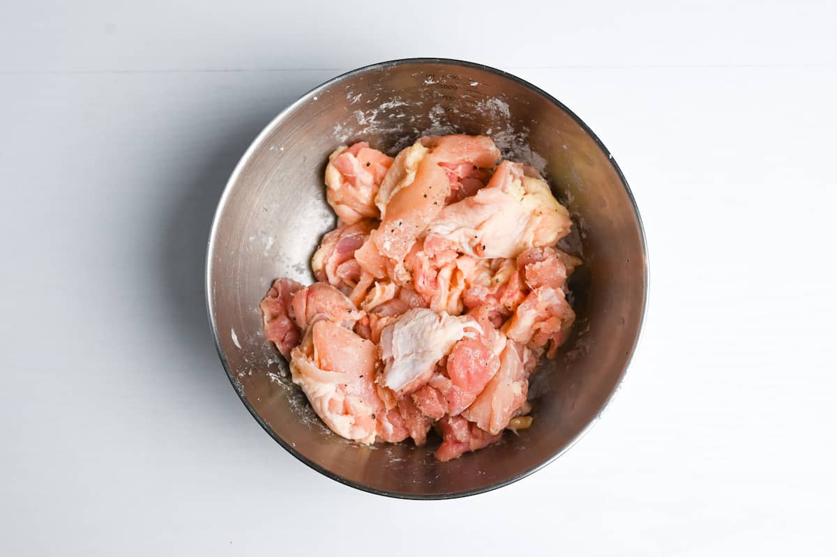 Chicken thigh coated with salt, pepper and starch in a metal bowl
