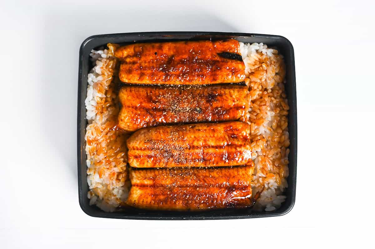 grilled eel coated with homemade unagi sauce and shansho pepper over rice in a black lacquerware box