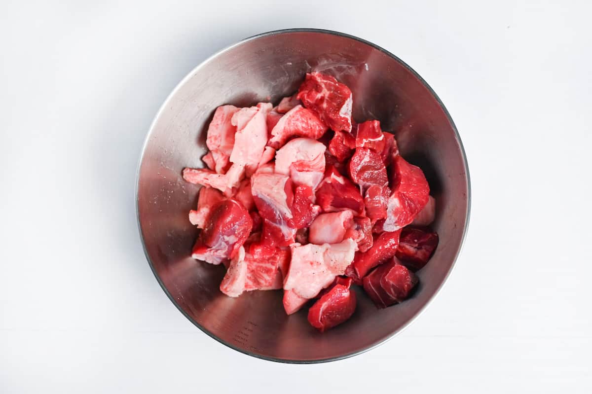 chunks of beef sprinkled with salt and pepper in a metal mixing bowl