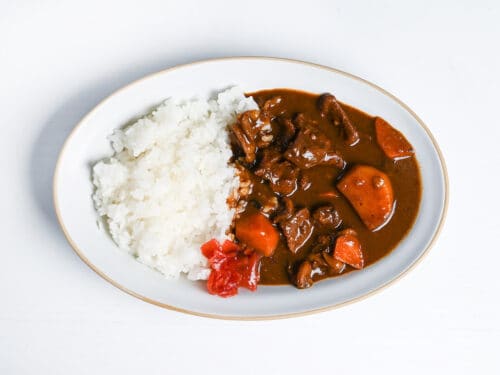 Homemade Japanese beef curry from scratch on a oval plate with rice and fukujinzuke pickles