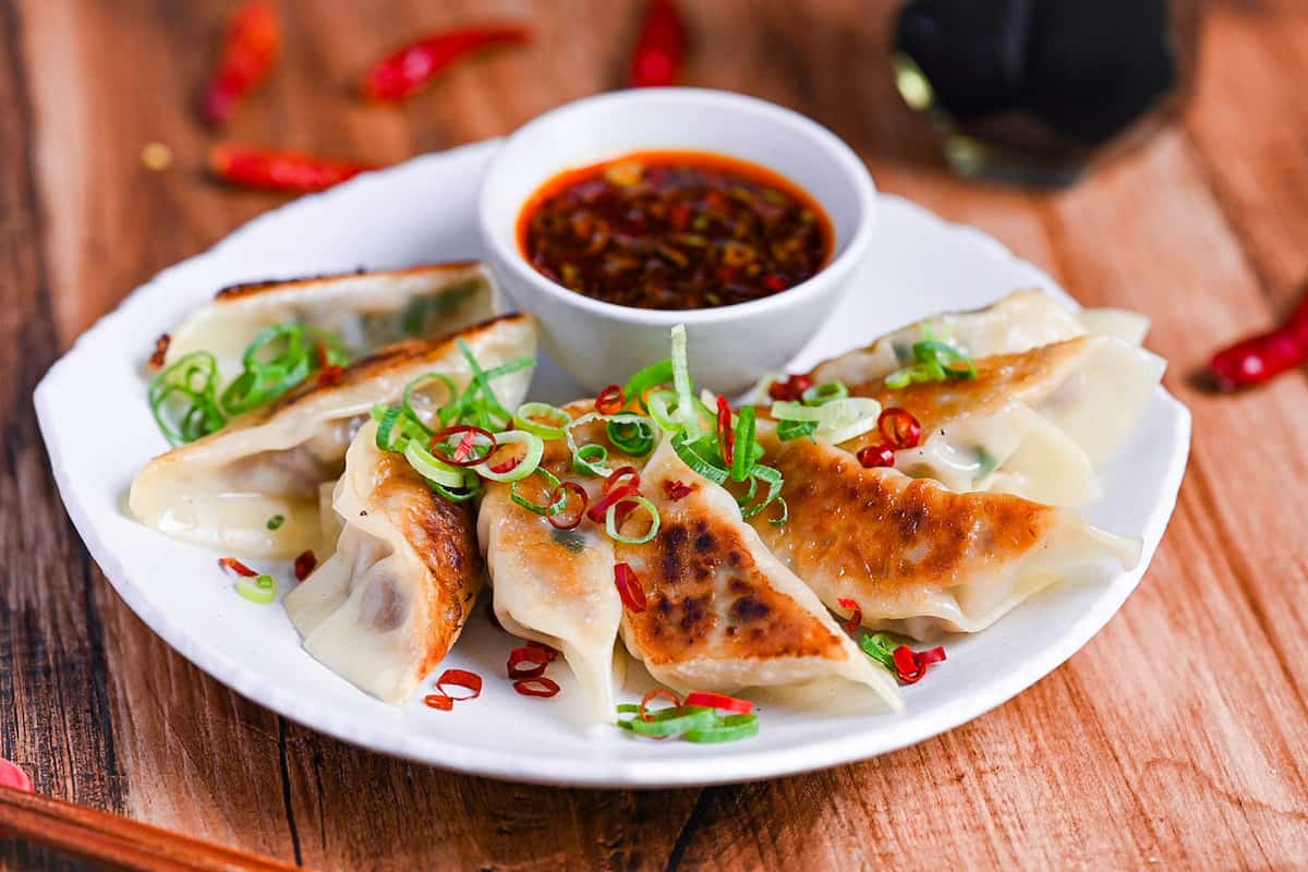 Spicy beef gyoza with hot dipping sauce sprinkled with chopped green onion and dry chilis on a white plate side view