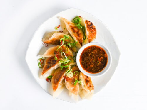 Spicy beef gyoza with hot dipping sauce sprinkled with chopped green onion and dry chilis on a white plate