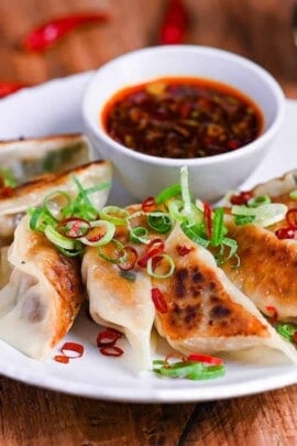 Spicy beef gyoza with hot dipping sauce sprinkled with chopped green onion and dry chilis on a white plate