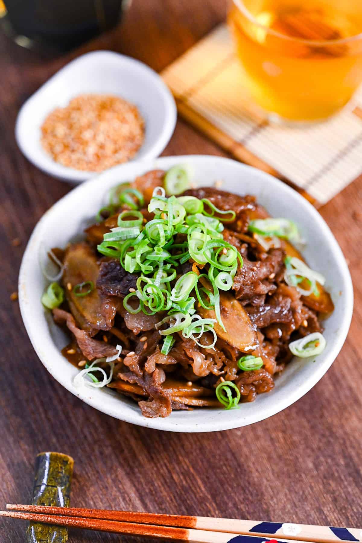 Beef shigureni with ginger and burdock root in a white dish topped with chopped green onion