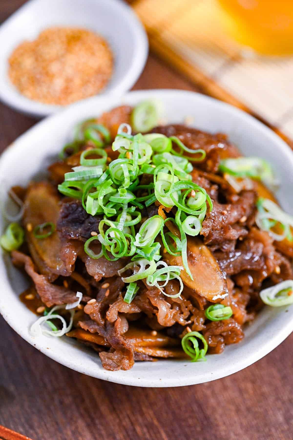 Beef shigureni with ginger and burdock root in a white dish topped with chopped green onion