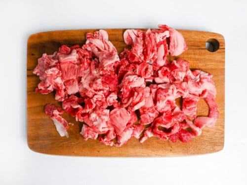 thinly sliced wagyu beef cut into 2cm pieces on a wooden chopping board