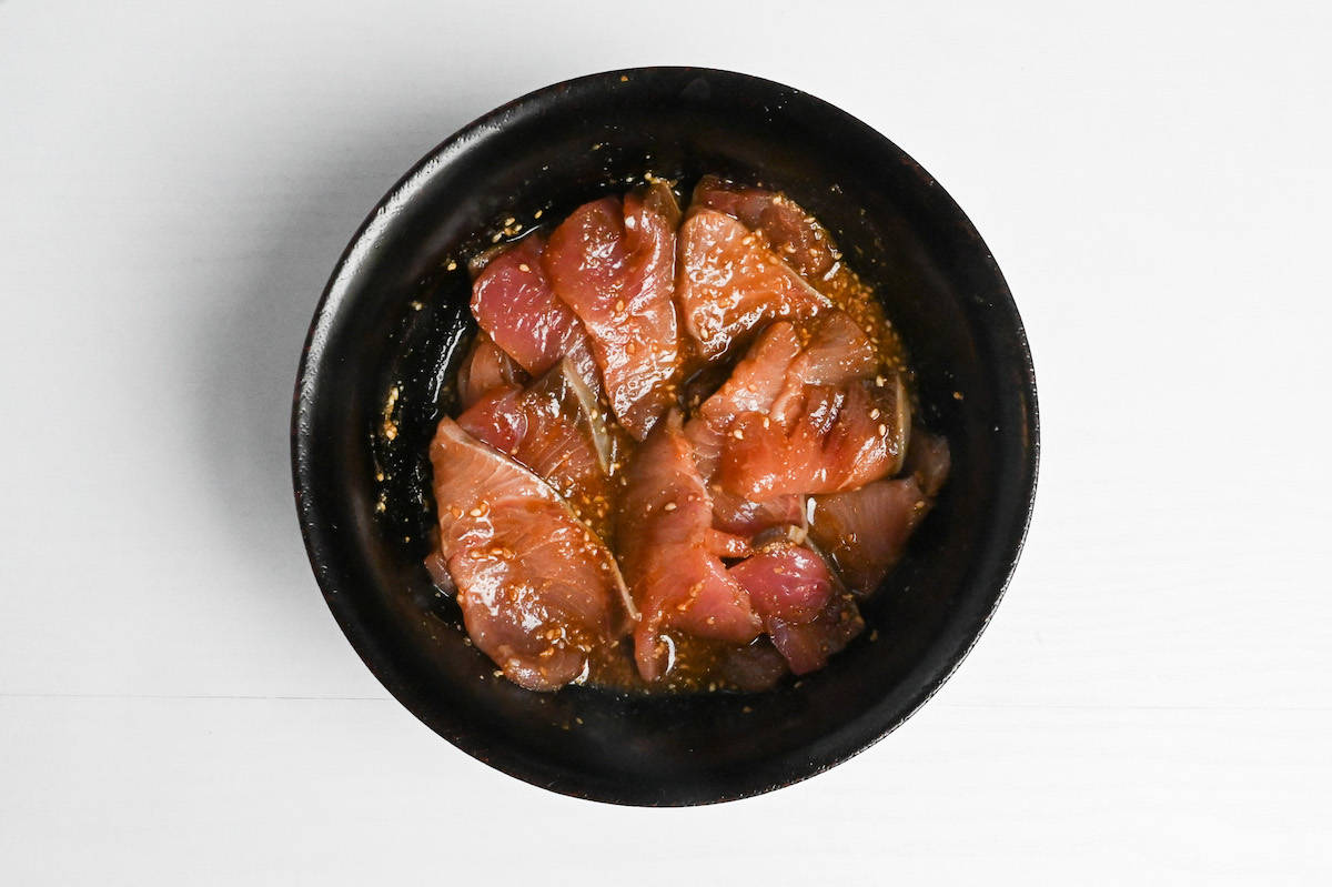 Yellowtail sashimi coated in marinade in a black bowl.