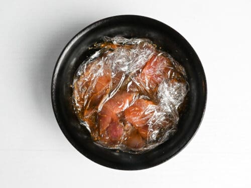 Yellowtail sashimi coated in marinade and covered with plastic wrap.