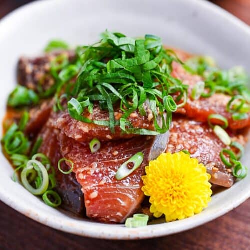 Marinated Yellowtail Sashimi (Buri no Ryukyu) in a small white bowl topped with sesame seeds, chopped green onion and shredded perilla leaves