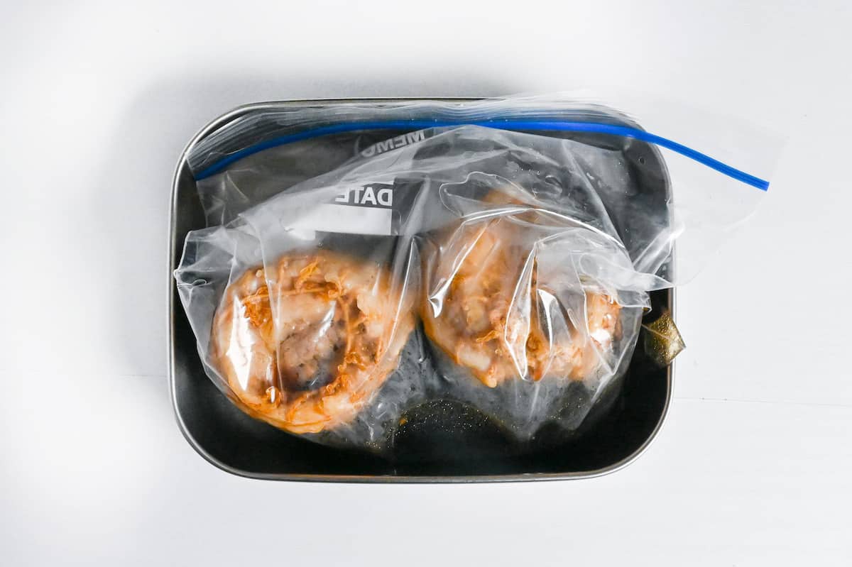 rolls of cooked pork belly soaking in a chashu marinade in a sealable freezer bag