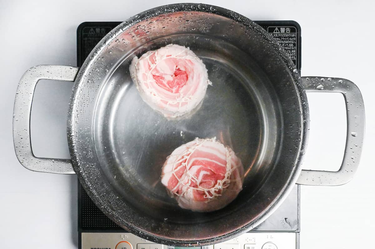 Two rolls of pork belly simmering in a large pot of water