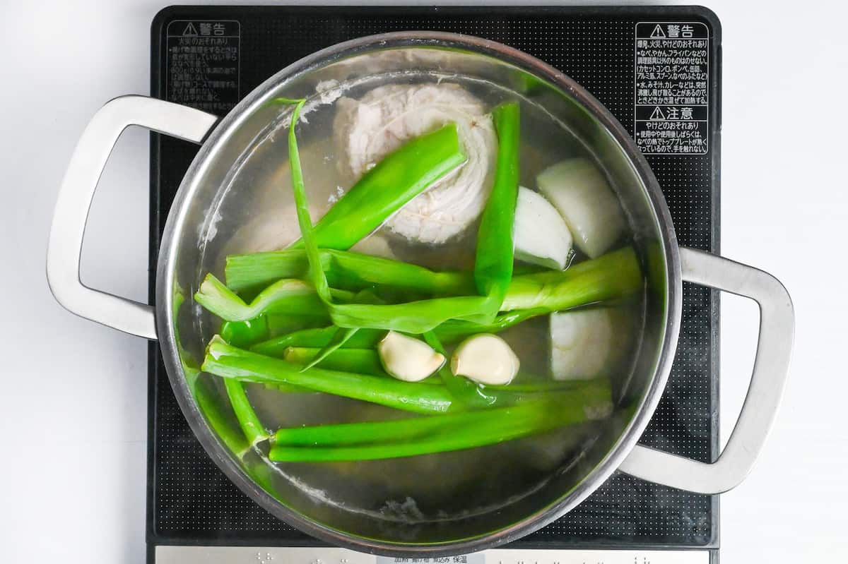 pork belly simmering in a pot with green onion, garlic cloves, onion and ginger