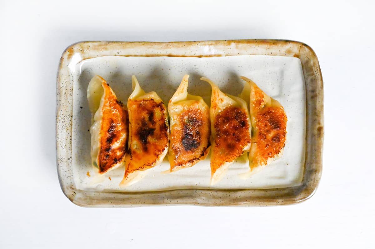 Chicken yaki gyoza flavored with umeboshi and perilla leaves layed out on a cream rectangular plate