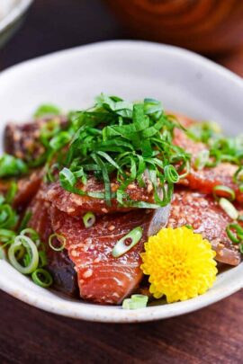Marinated Yellowtail Sashimi (Buri no Ryukyu) in a small white bowl topped with sesame seeds, chopped green onion and shredded perilla leaves