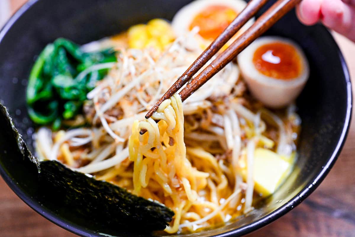 holding ramen noodles from a bowl of homemade pork miso ramen with wooden chopsticks