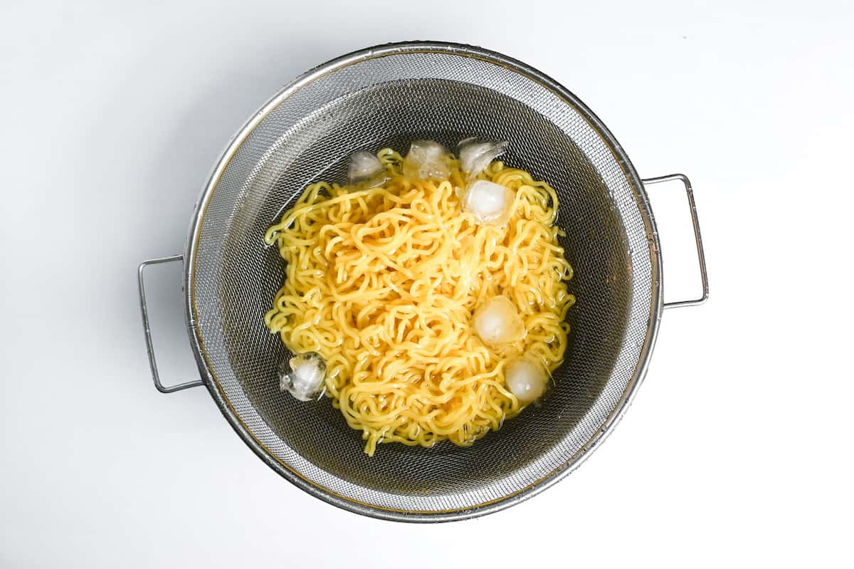 chilling ramen noodles with cold water and ice in a fine mesh sieve
