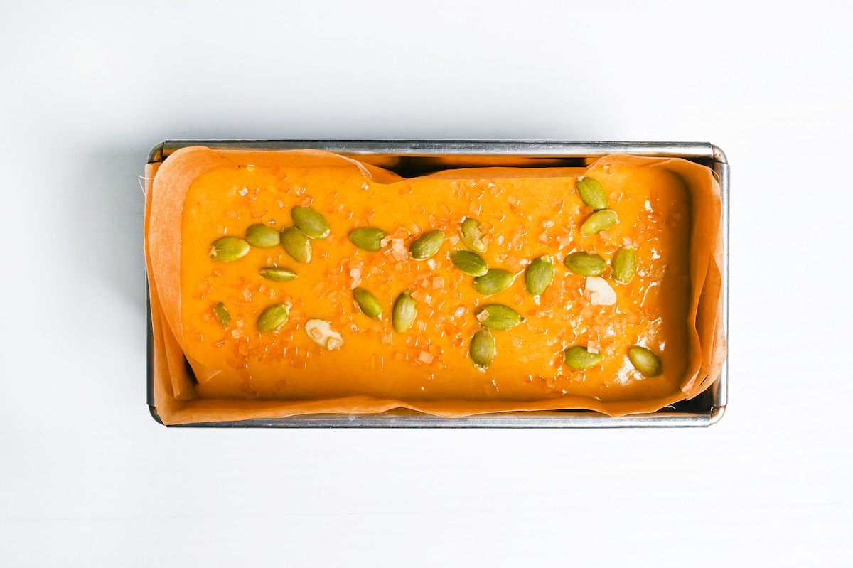 kabocha loaf batter in a line loaf pan topped with pumpkin seeds and turbinado sugar