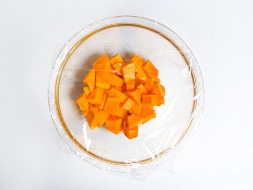 cubes of kabocha in a glass bowl covered with plastic wrap