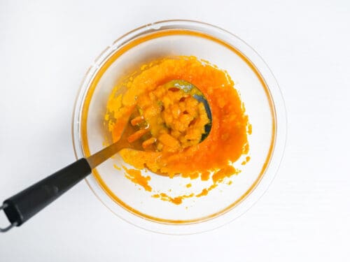 mashed kabocha in a glass bowl with potato masher